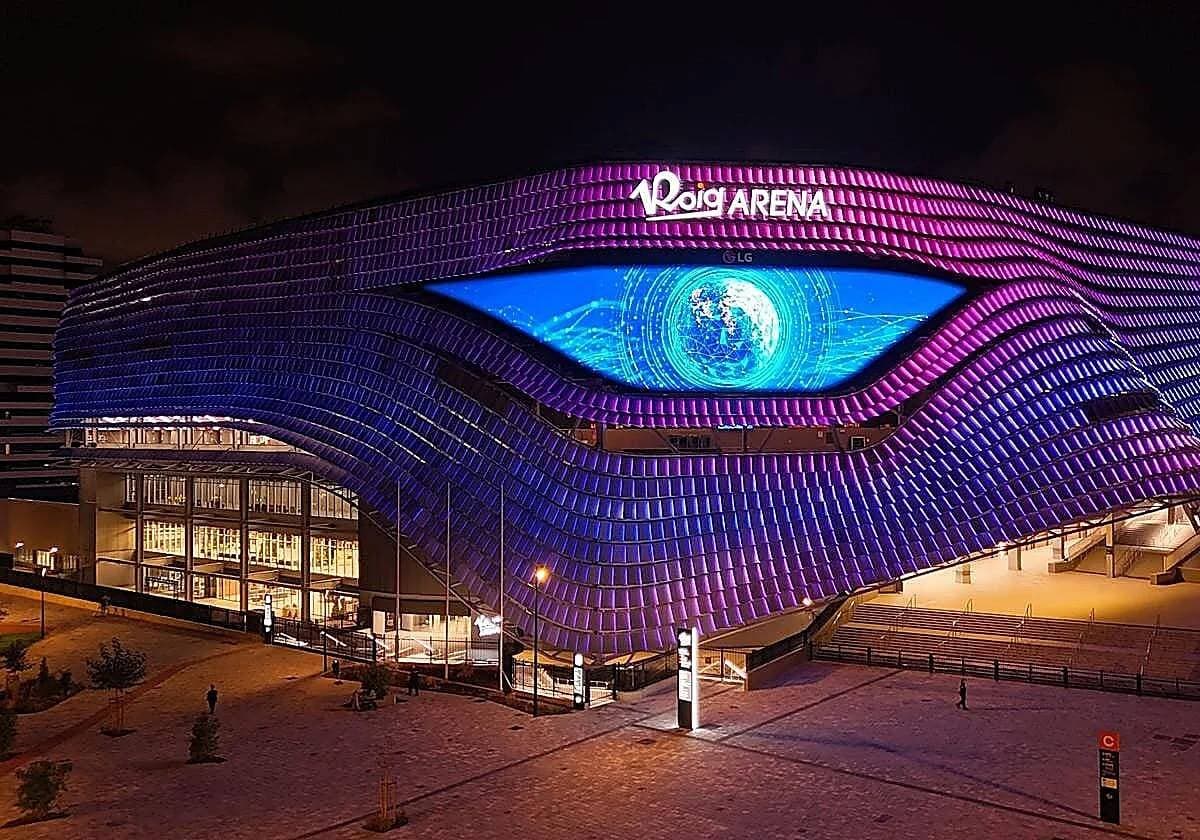 Vista nocturna del Roig Arena iluminado en tonos morados y azules.